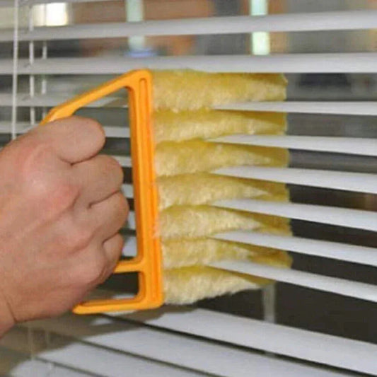 Person using a yellow brush with an orange handle to clean blinds.