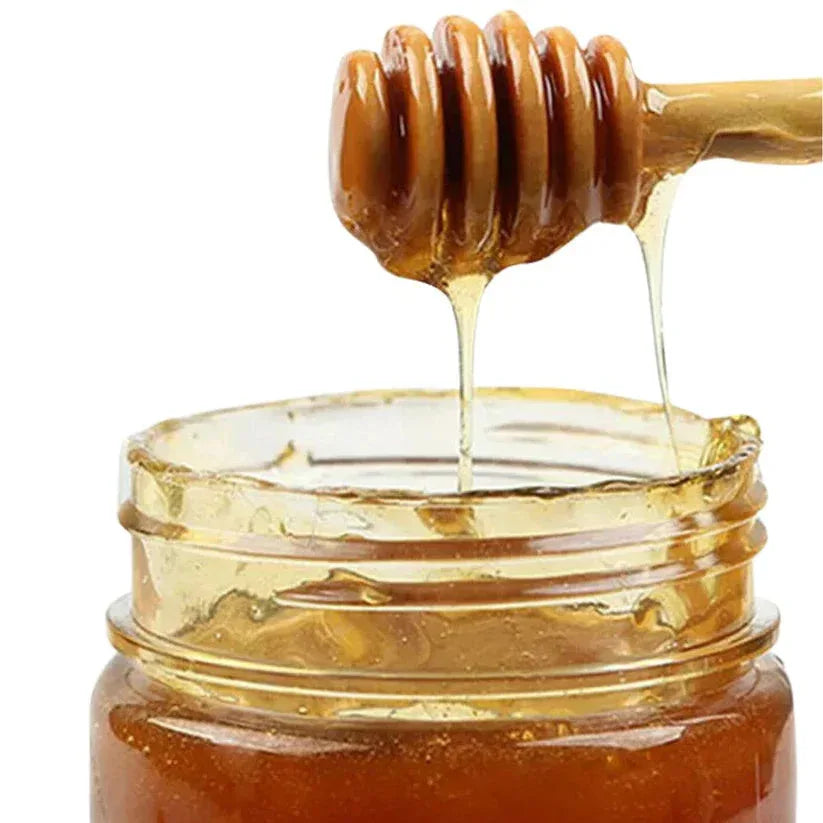 Honey dipper dripping honey into a jar on a white background