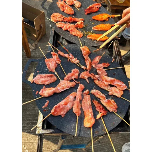 Skewered meat being grilled on a hotplate with a person using chopsticks.