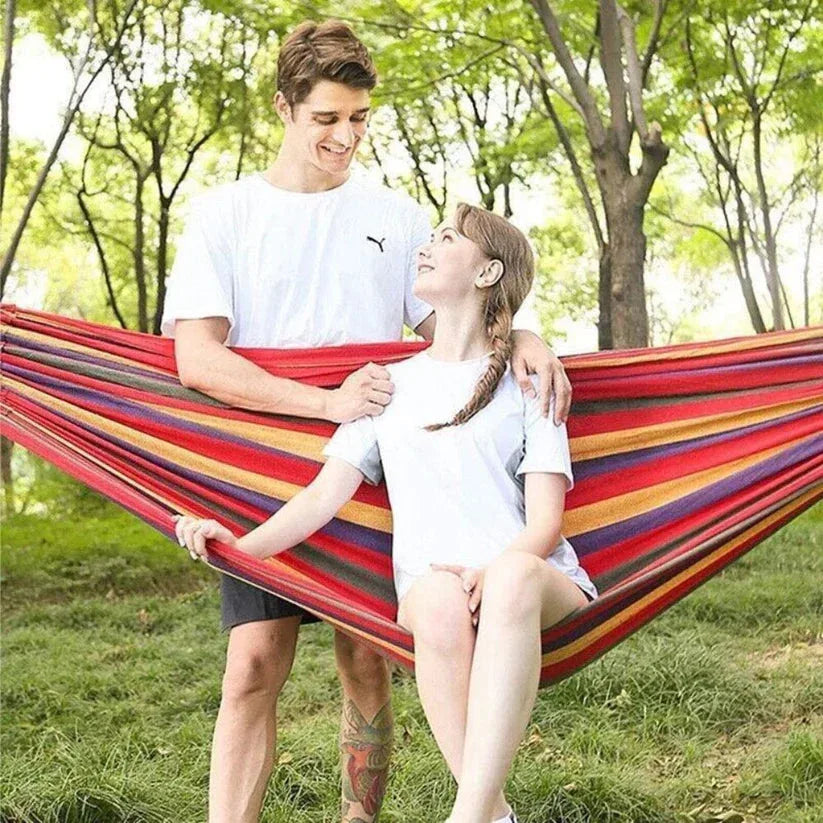 Two people in a colorful striped hammock surrounded by trees.