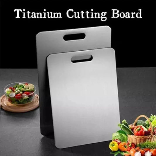 Two titanium cutting boards with handles on a dark surface, surrounded by vegetables and a salad.