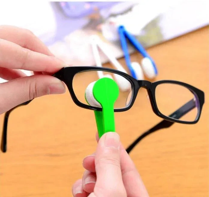 Person cleaning glasses with a green cleaning tool on a wooden surface