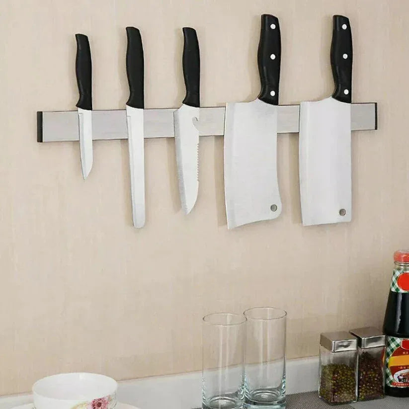 Set of knives on a magnetic wall strip above a kitchen counter with glasses and a bottle.


