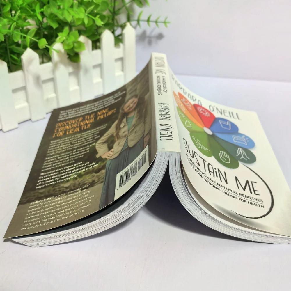 Two books open on a white surface with a plant in the background

