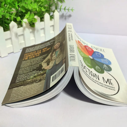 Two books open on a white surface with a plant in the background

