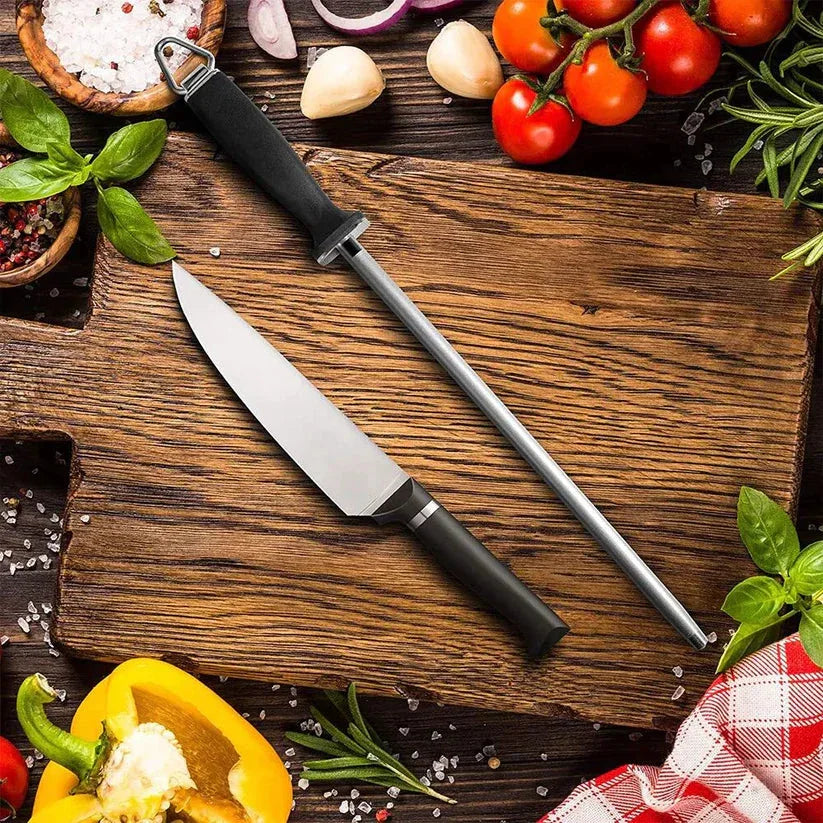 Knife and sharpener on a wooden cutting board with vegetables and herbs.

