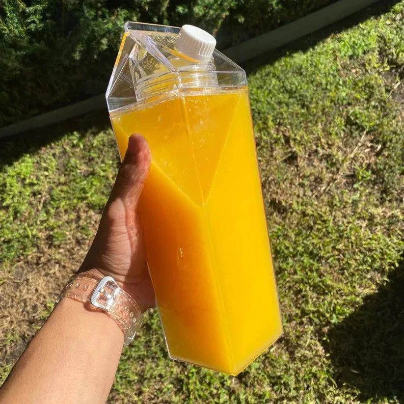 Hand holding a carton of orange juice with a grassy background

