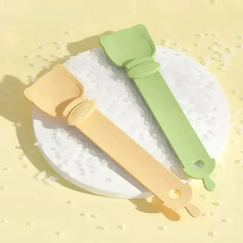 Two silicone brushes, one beige and one green, on a white plate with a yellow background.

