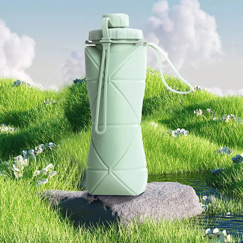 Collapsible green water bottle on a rock with a grassy background

