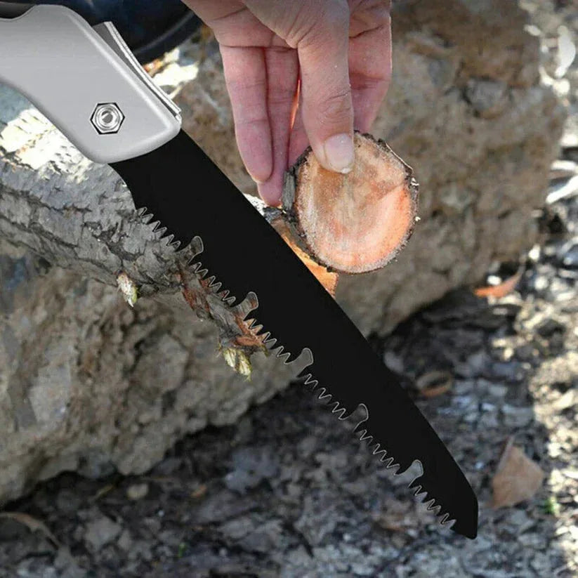 Hand holding a folding saw cutting through wood with a natural outdoor background

