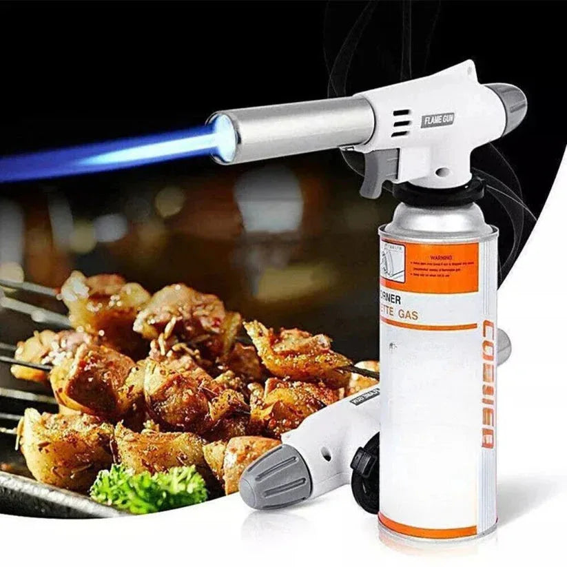 Butane gas torch being used to cook meat on a grill with a blurred background

