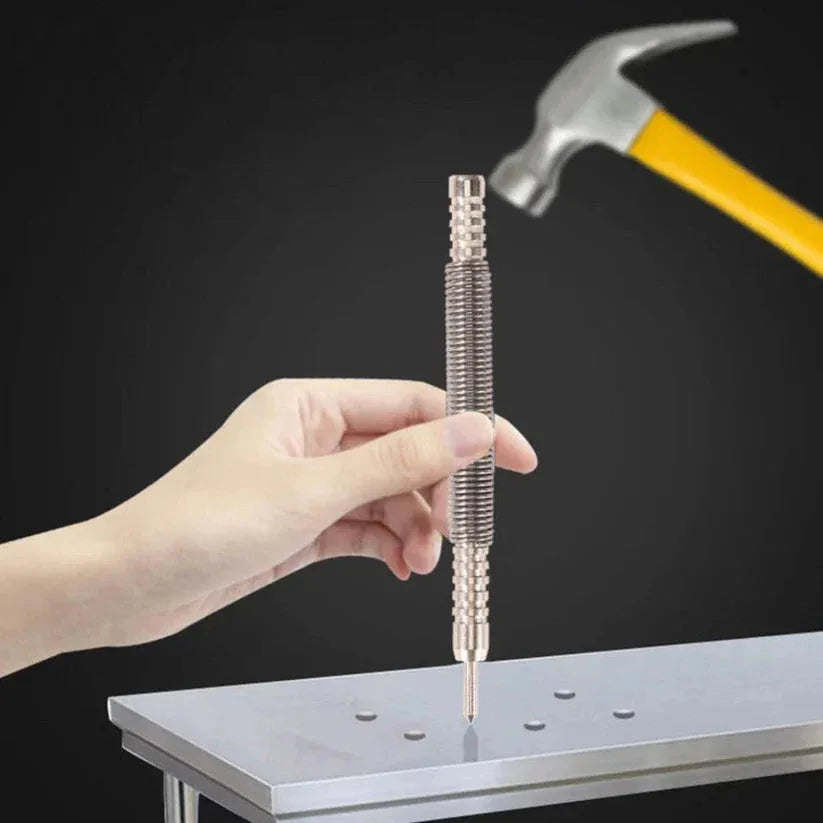Hand holding a small metal tool above a metal surface with a hammer in the background.

