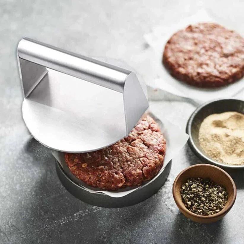 Hamburger press being used to shape ground meat on a gray surface with spices in small bowls.

