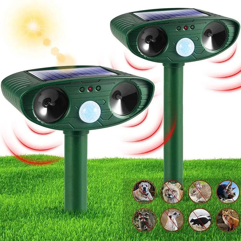 Two solar-powered animal deterrent devices on grass with a sun in the background.

