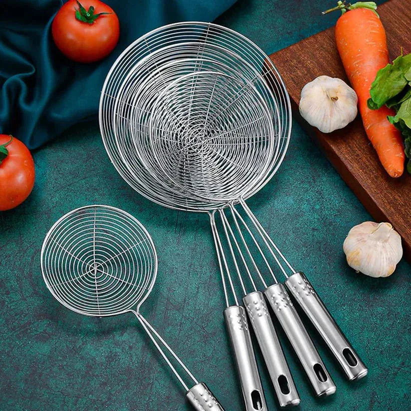 Set of metal ladles on a green surface with vegetables in the background

