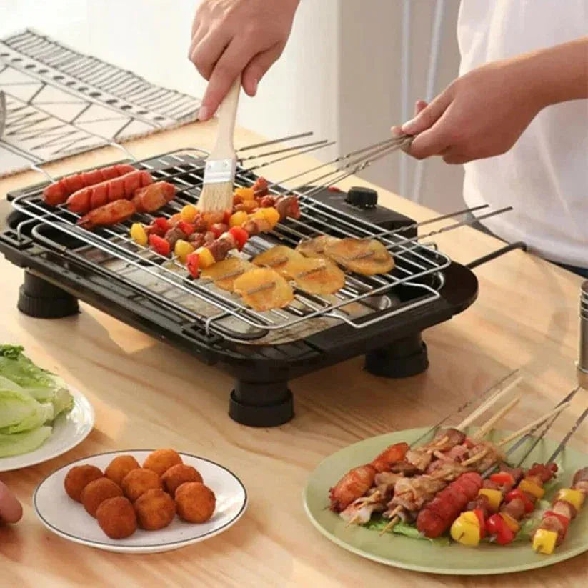 Person grilling food on a small portable grill with skewers on a wooden table.

