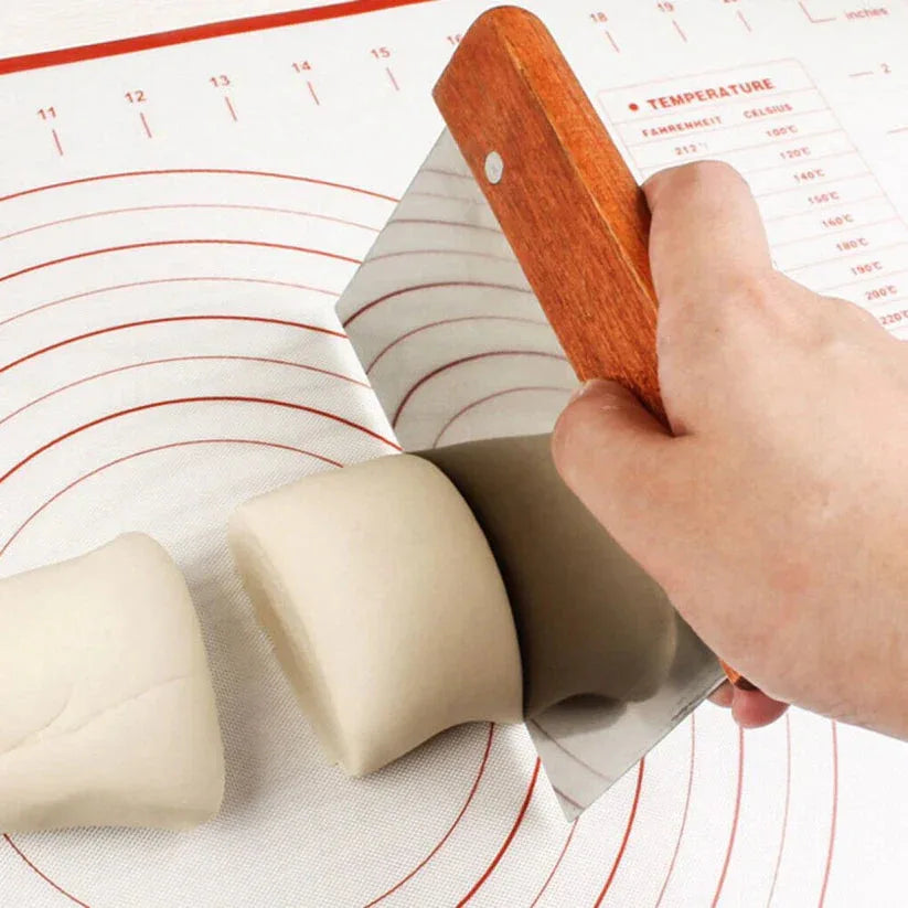 Hand using a dough scraper on kneaded dough with a temperature gauge in the background

