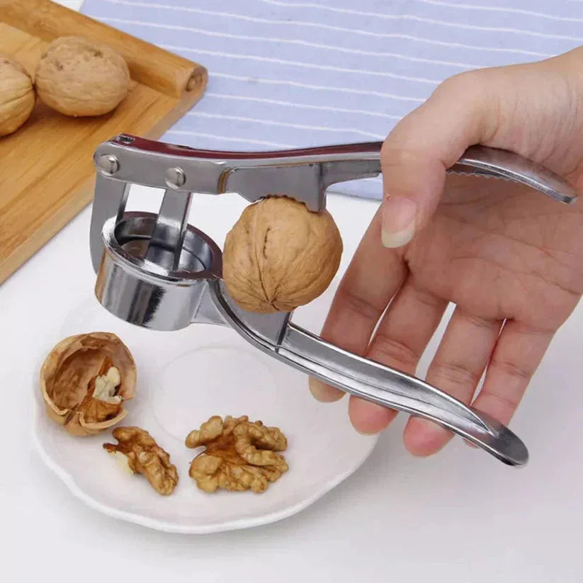 Hand using a metal nutcracker to open a walnut on a white plate with other walnuts.

