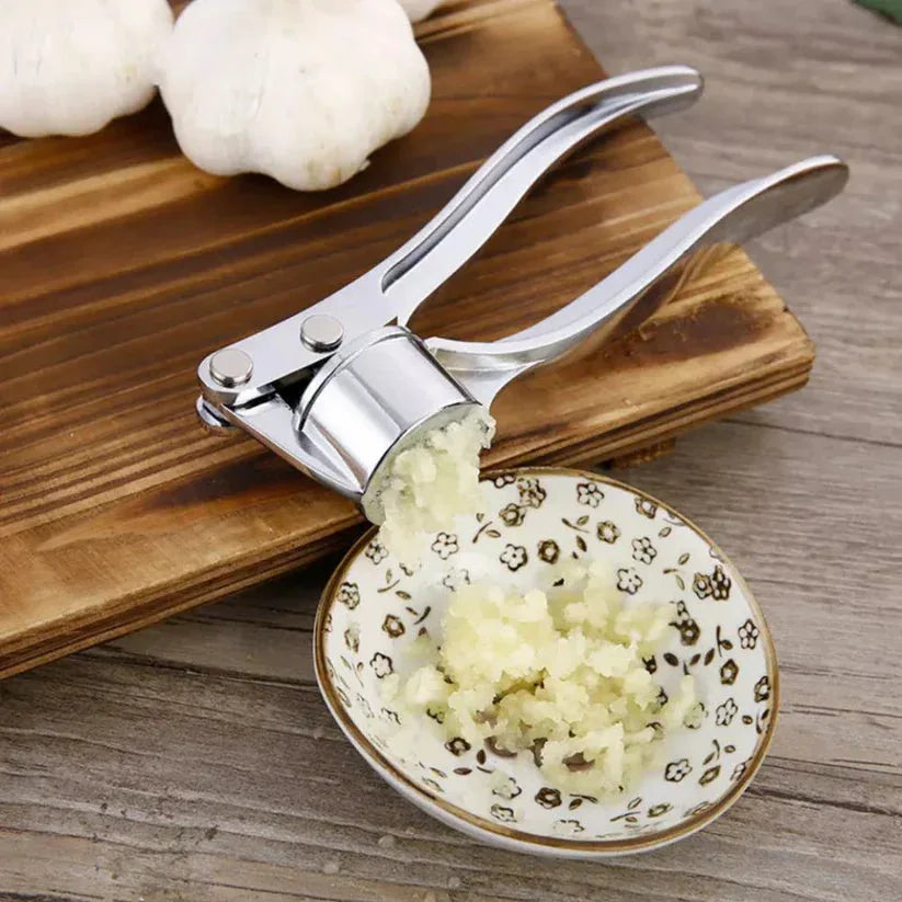 Garlic press with minced garlic on a small plate on a wooden surface

