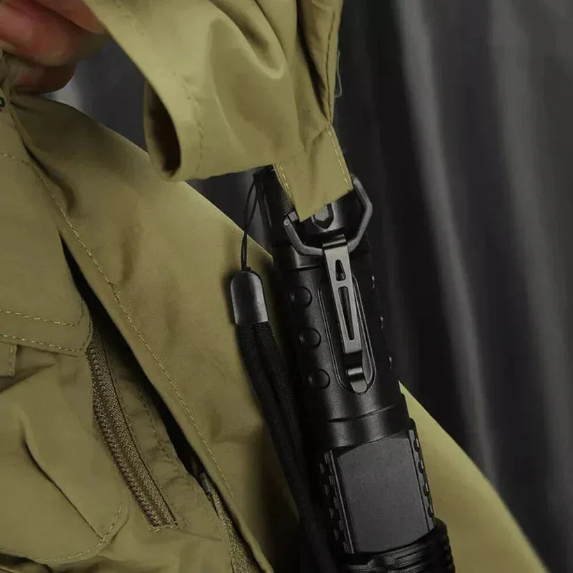 Person wearing a green jacket holding a black flashlight against a dark background

