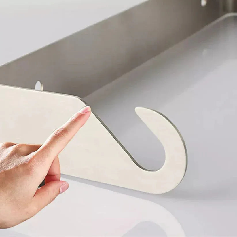 Hand holding a white cutting board with a silver U-shaped hook over a sink.

